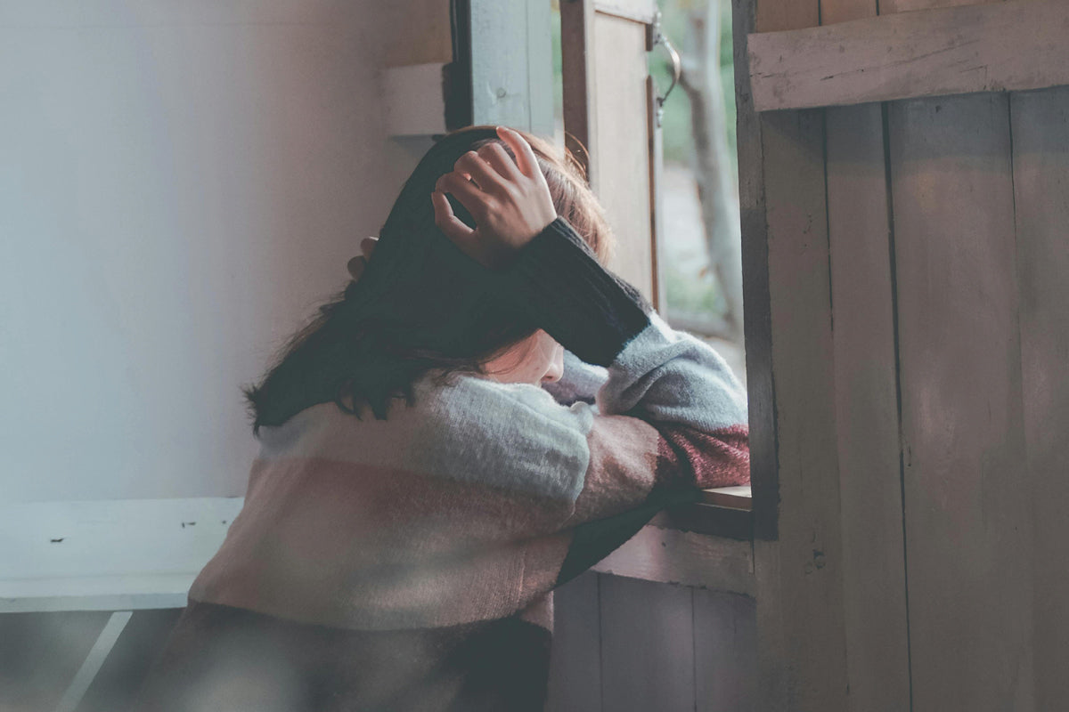 A woman leans on the window, her hand covering her head, appearing stressed.