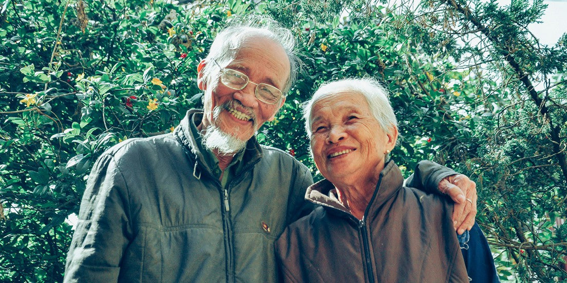 An elderly couple smiling in front of a botanical tree, exemplifying healthy aging.